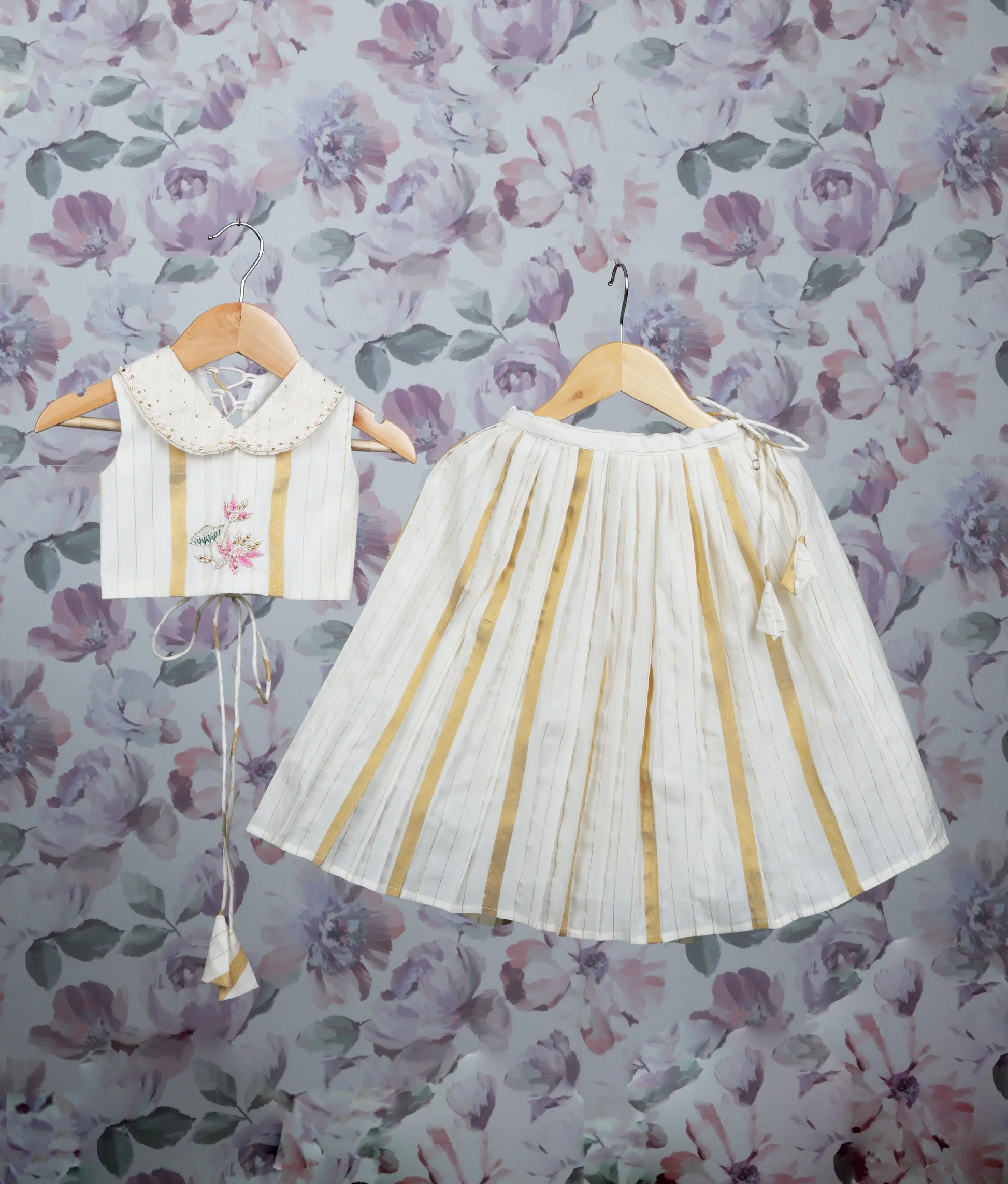 Off-white and gold pleated skirt set with a handworked top on a hanger.