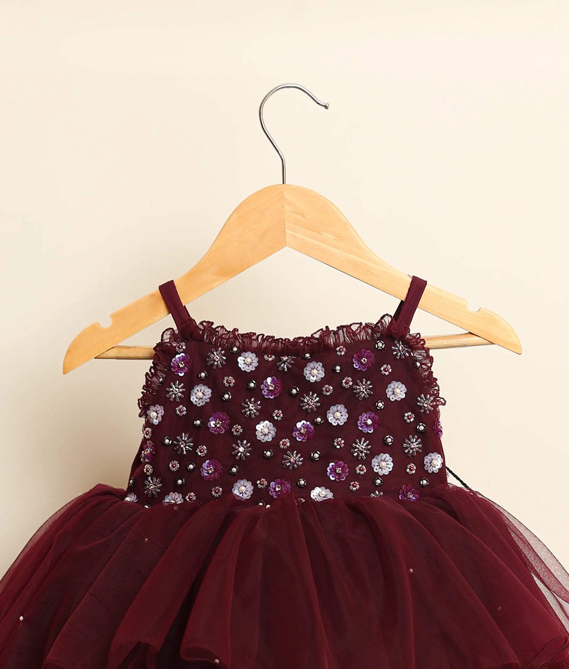 Close view of a wine-red tulle net handworked high-low birthday frock against plain background