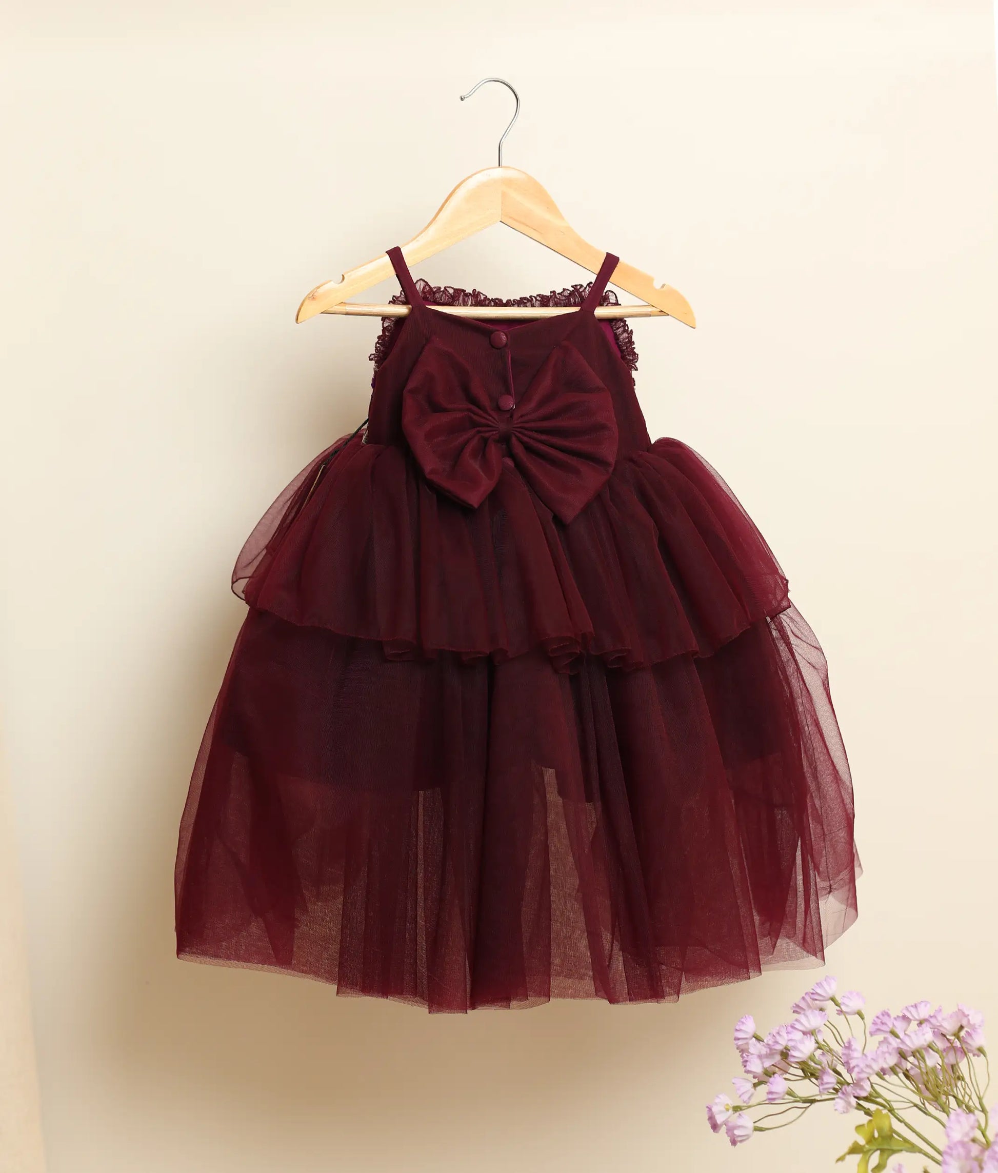 Back view of a wine-red tulle net handworked high-low birthday frock against plain background