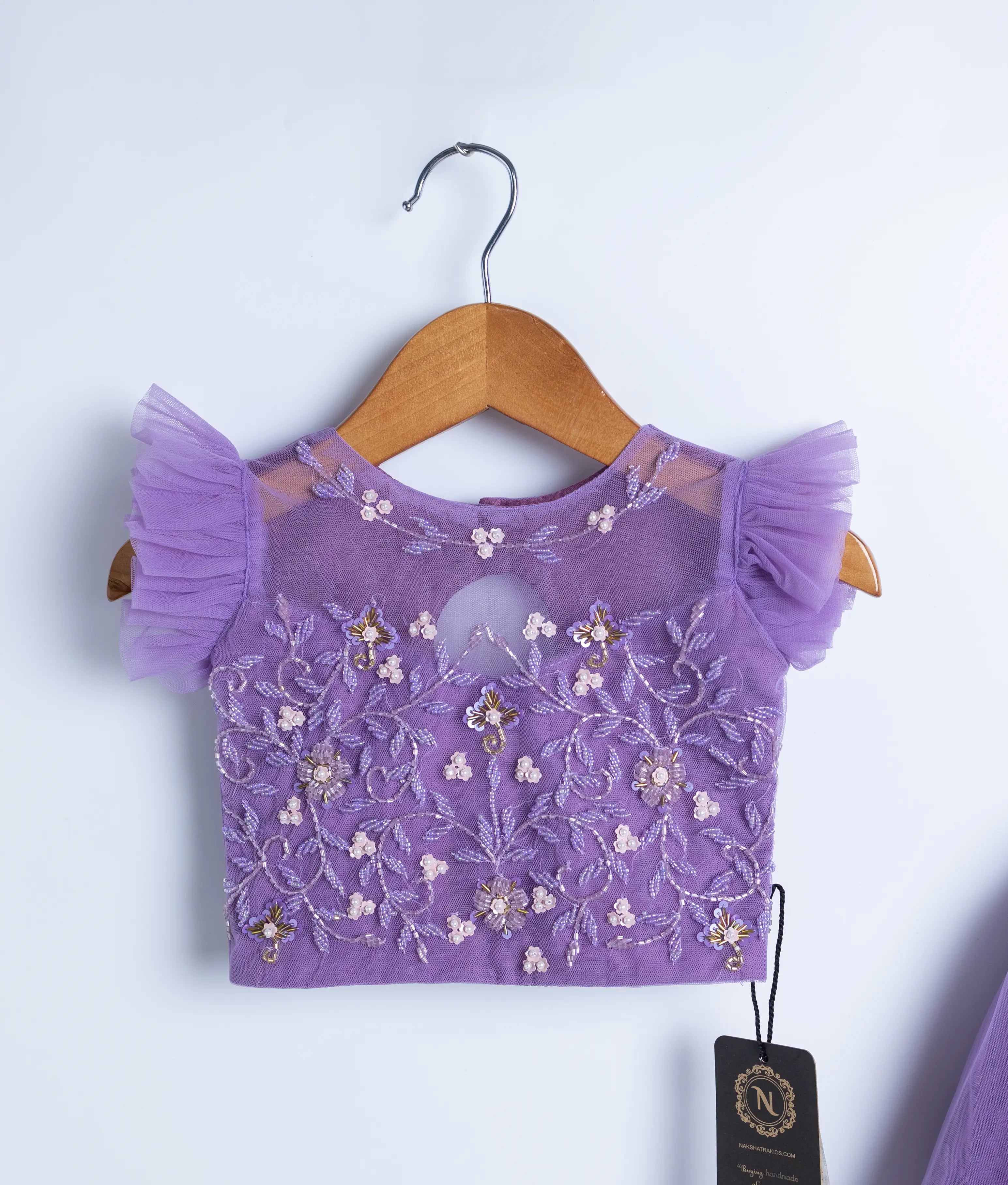 Close view of an lavender crop top and full-length skirt on wooden hangers against a white background.