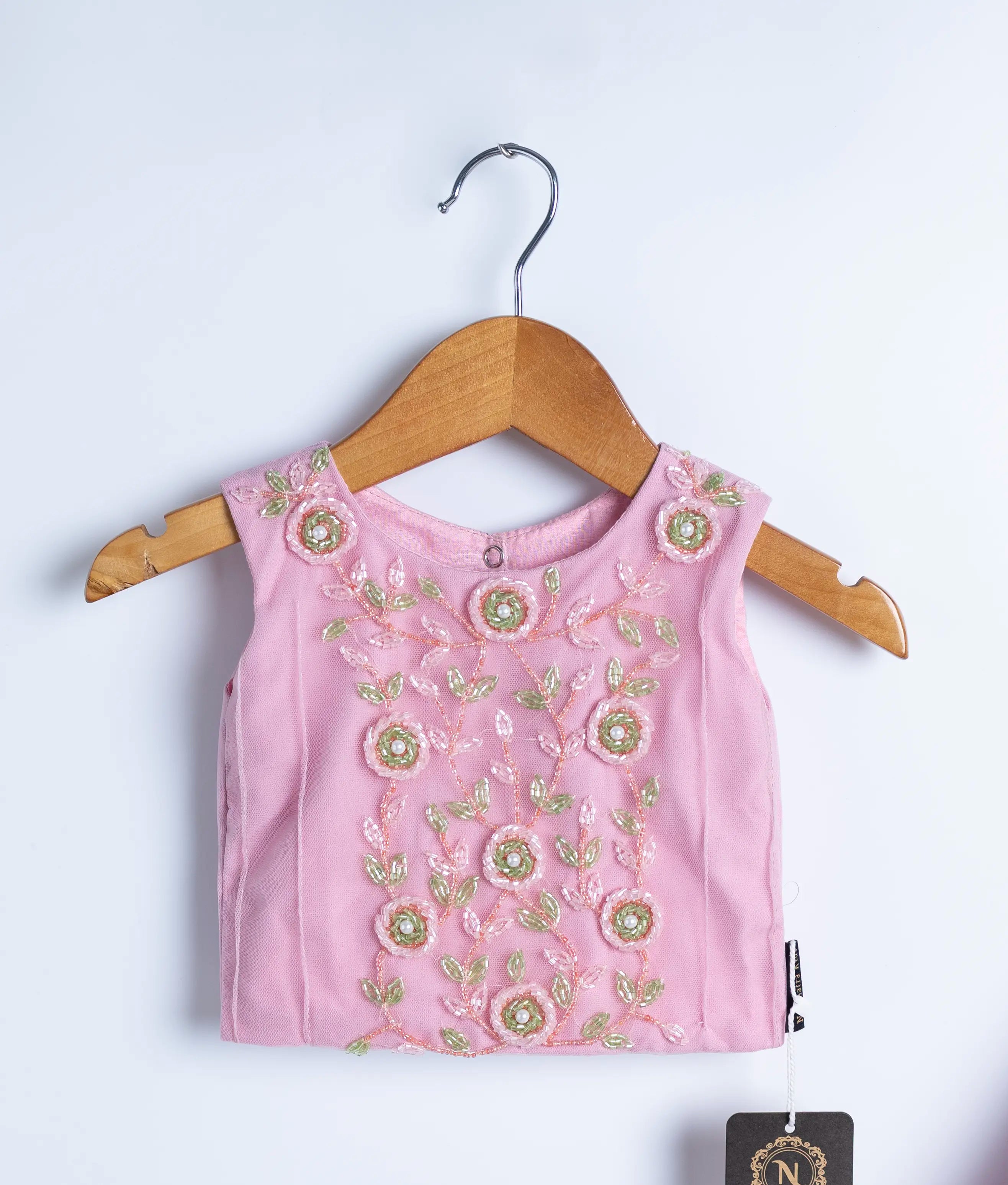 Close view of an pink crop top with handwork displayed on wooden hanger.