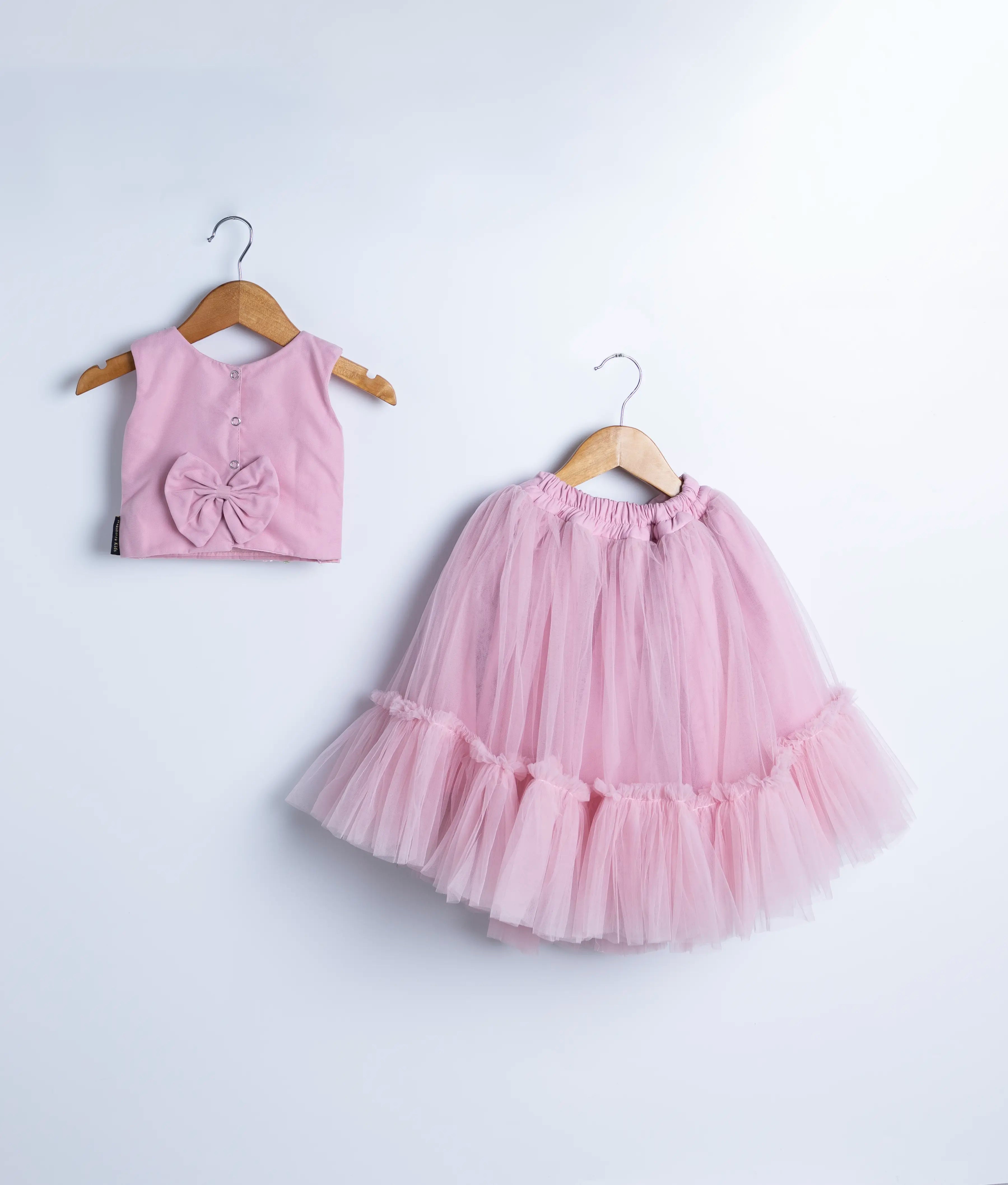 Back view of an pink crop top with handwork and a full-length pink skirt displayed on wooden hangers against a white background.