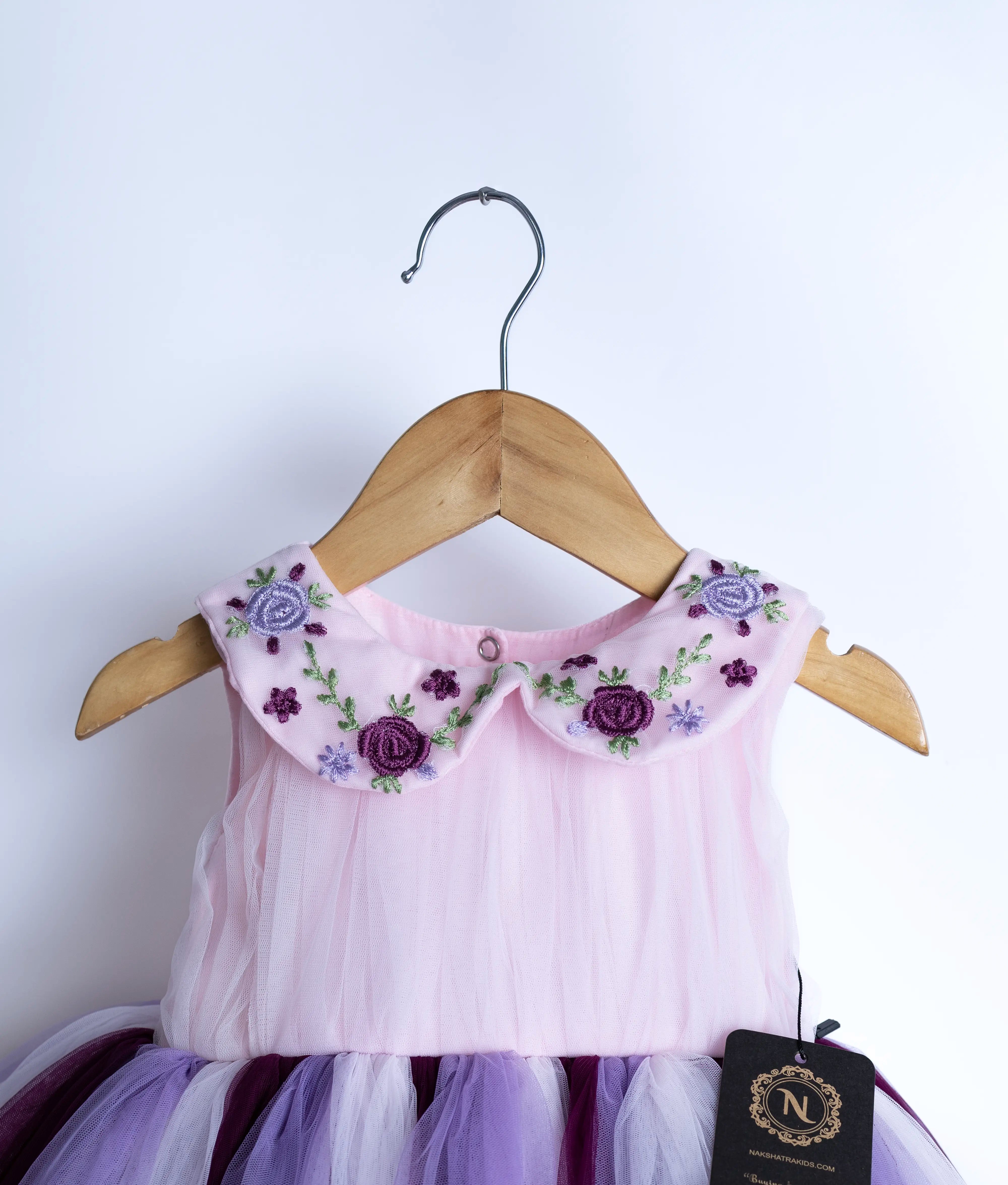 Close view of an sleeveless birthday frock hanging on a hanger against a white background.