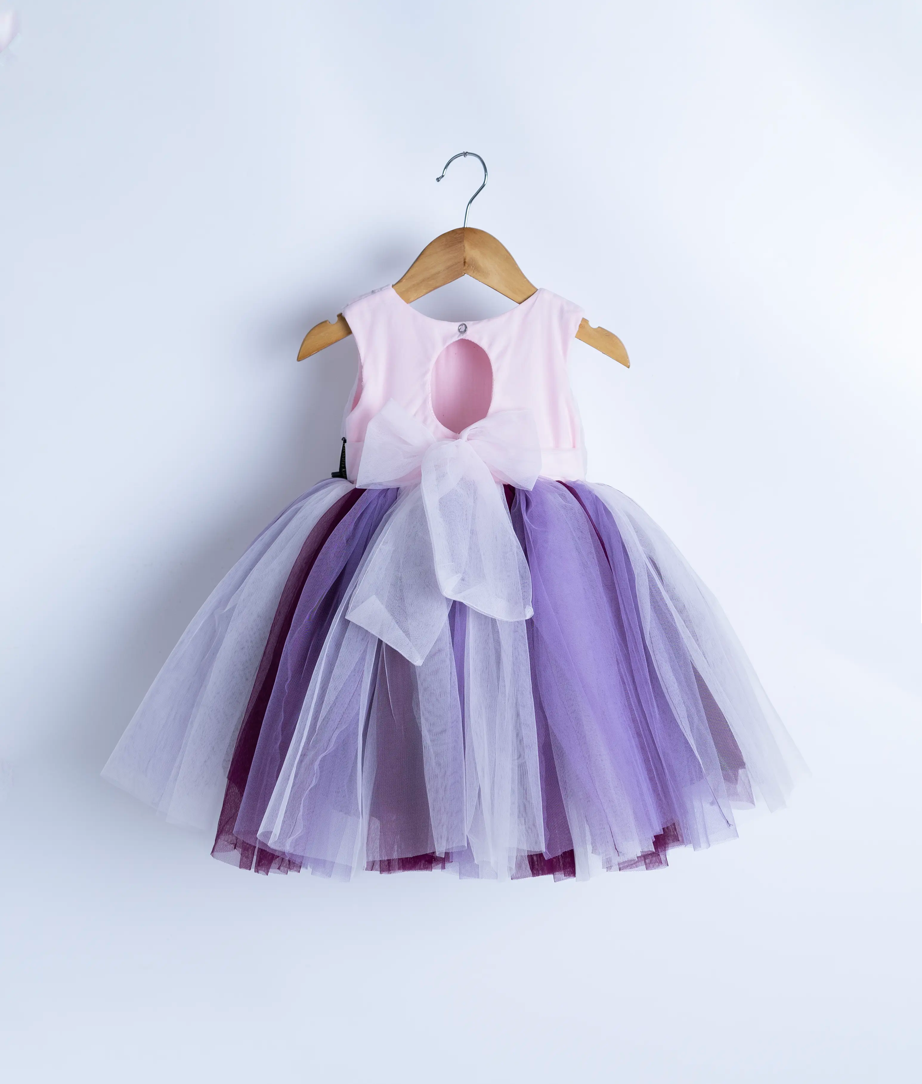 Back view of an sleeveless birthday frock hanging on a hanger against a white background.