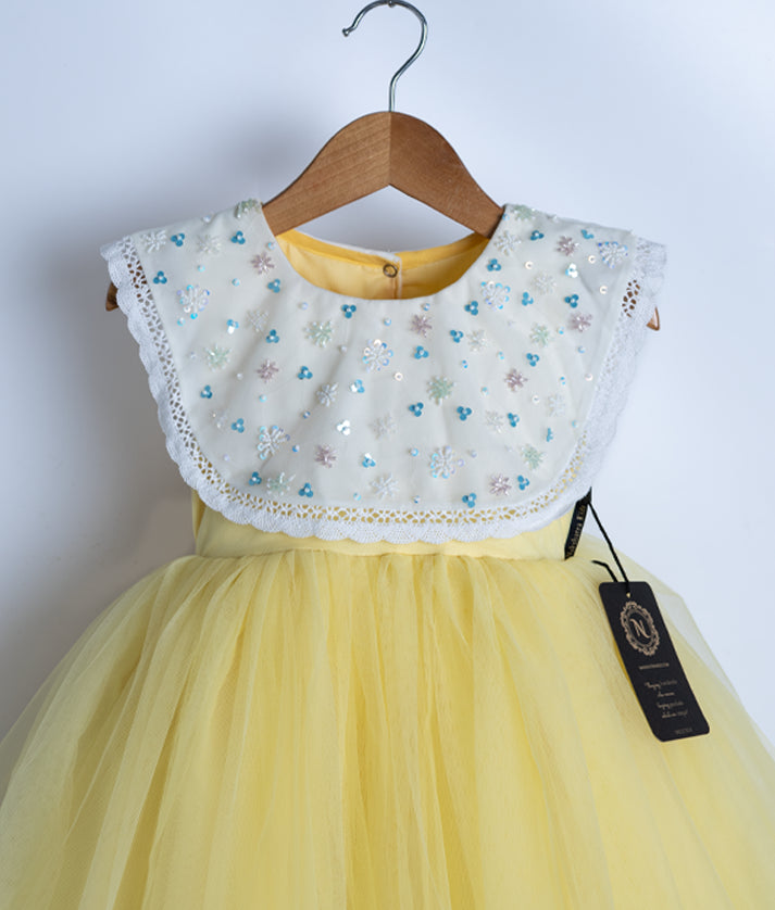Close view of an off-white and yellow frock displayed on a hanger.
