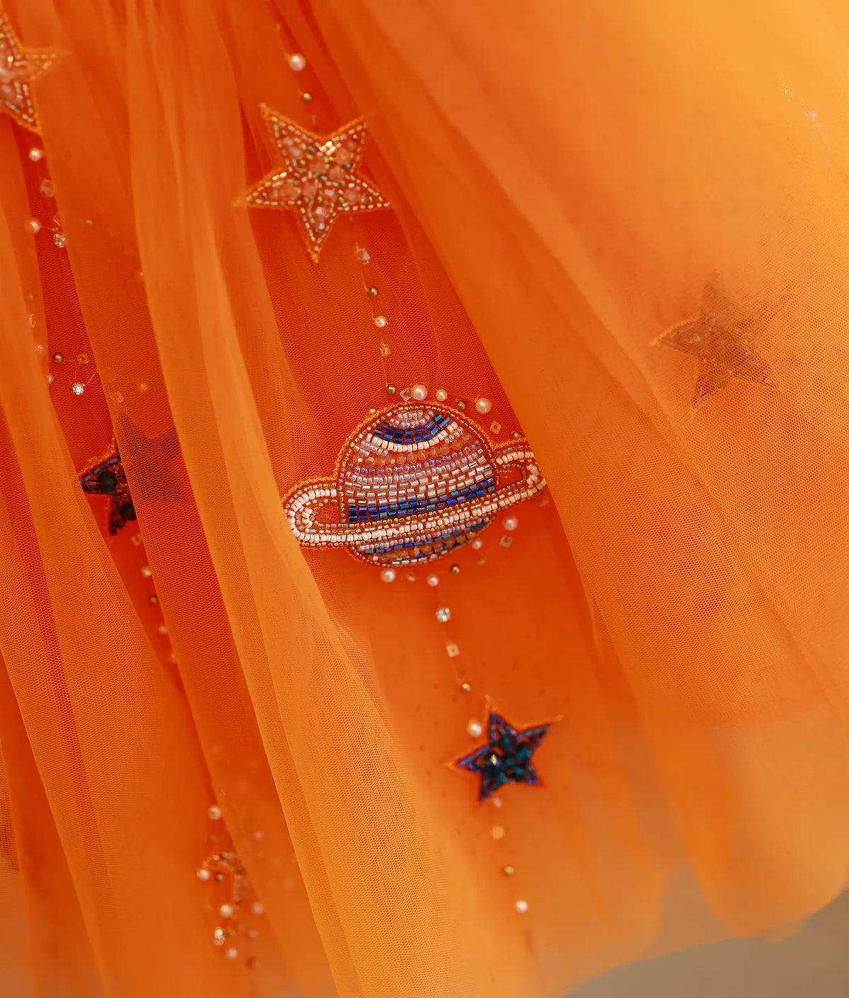 Close-up view of orange net skirt showing handworked planet and sparkling star motifs.