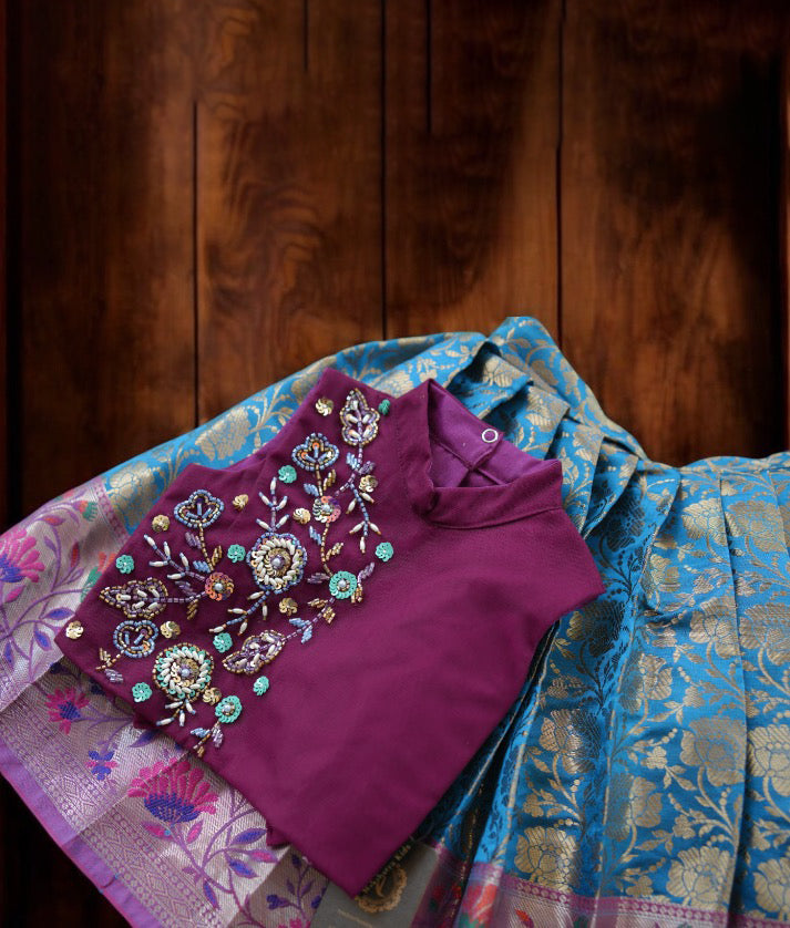 Close view of an grape wine and blue handworked crop top paired with a banarasi skirt, displayed on a wooden surface.