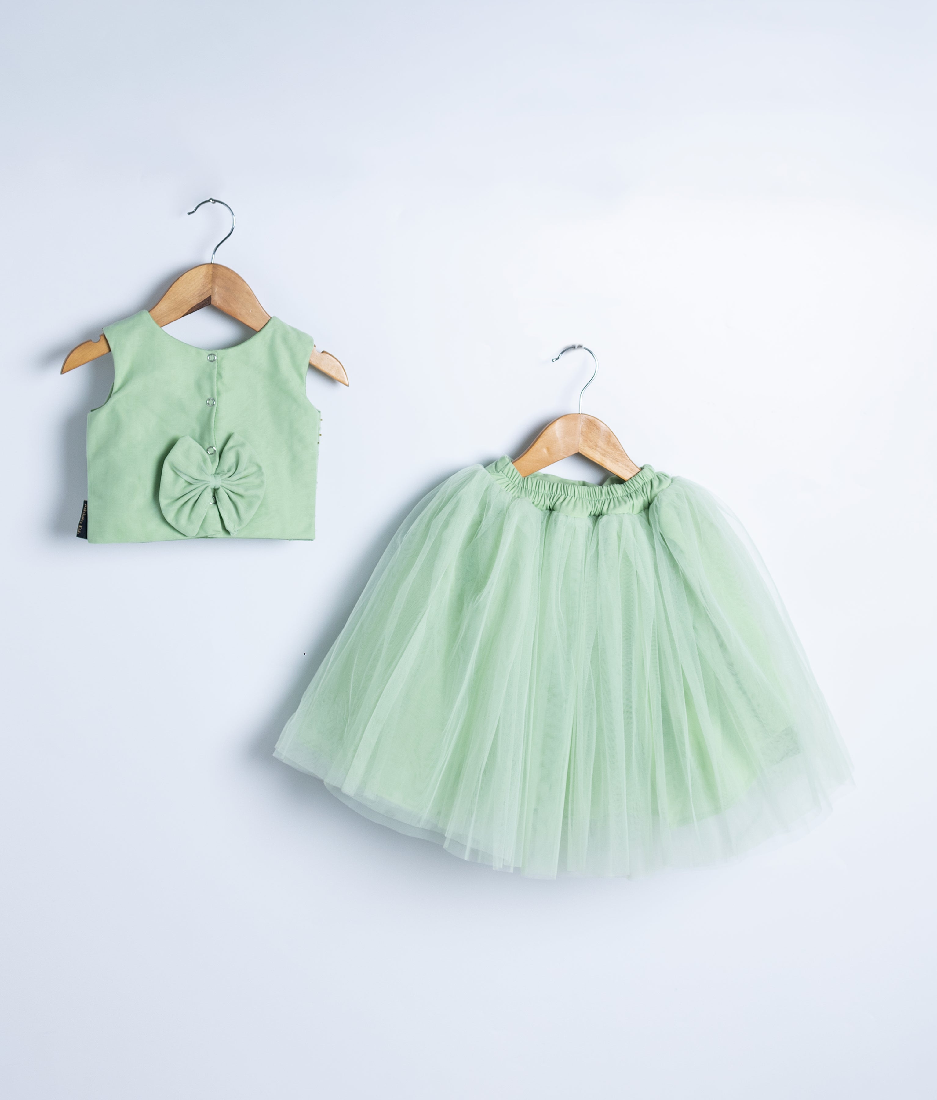 Back view of an pastel green crop top and a skirt displayed on a wooden hangers.