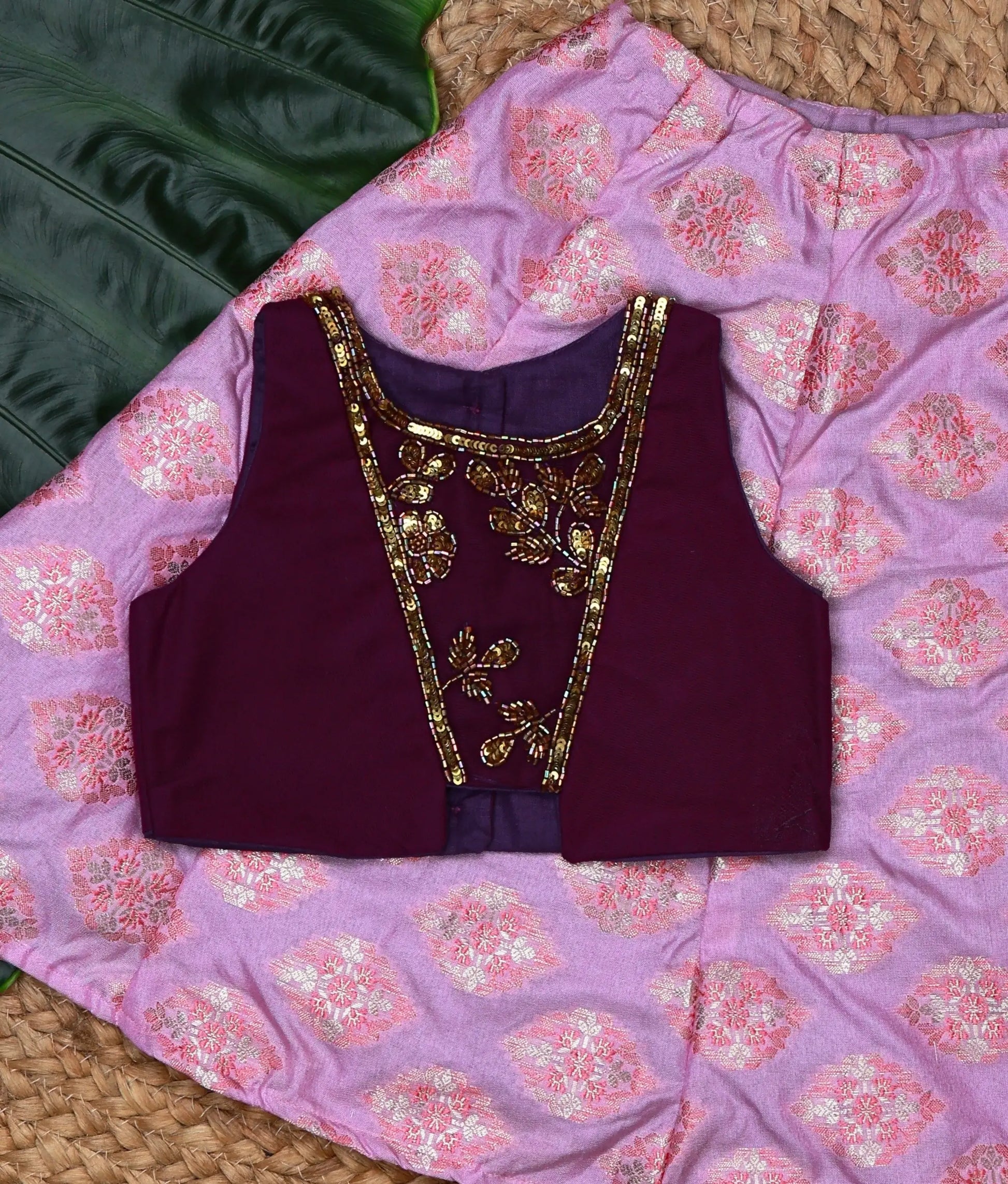 Close view of a traditional kids lehenga set featuring a purple handworked sleeveless top and a pink brocade skirt with gold motifs.