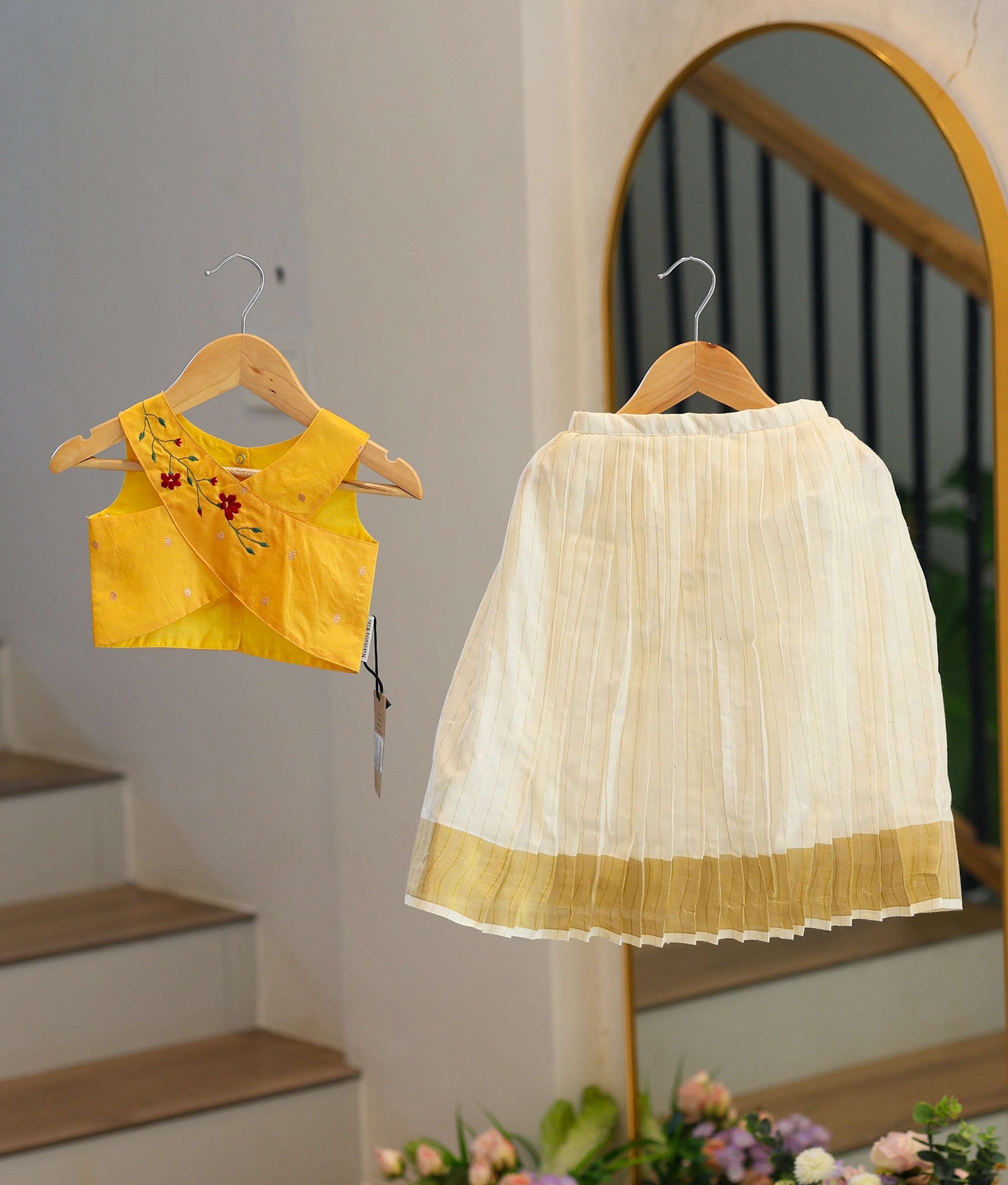 Front view of a girls' yellow top with floral embroidery and a kasavu pleated skirt with vertical stripes.