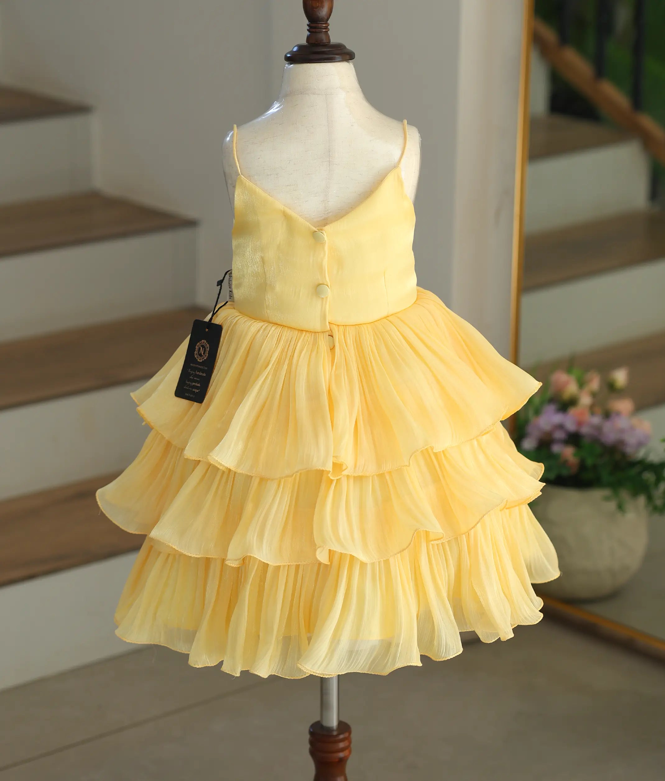 Back view of the yellow tiered laser organza dress showing the button closure and simple V-neck design.