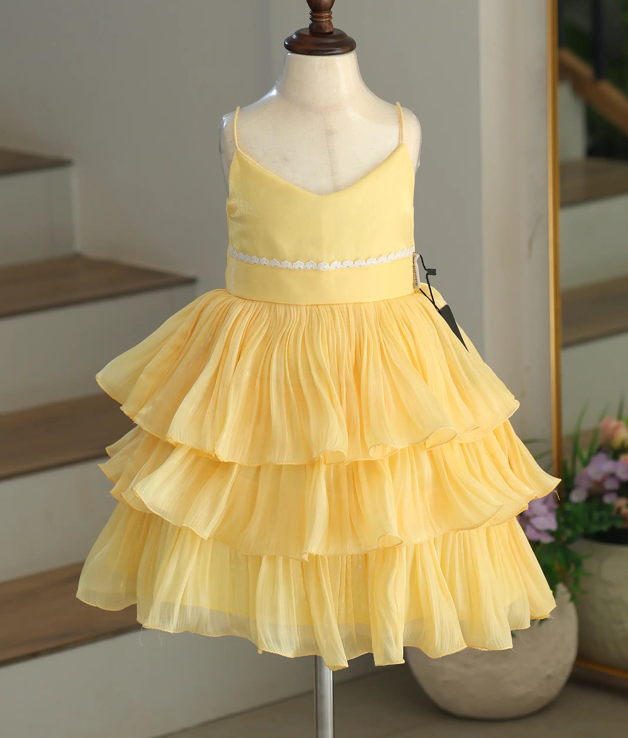 Front view of a bright yellow tiered frock for girls made of shimmery laser organza with a white lace waist.