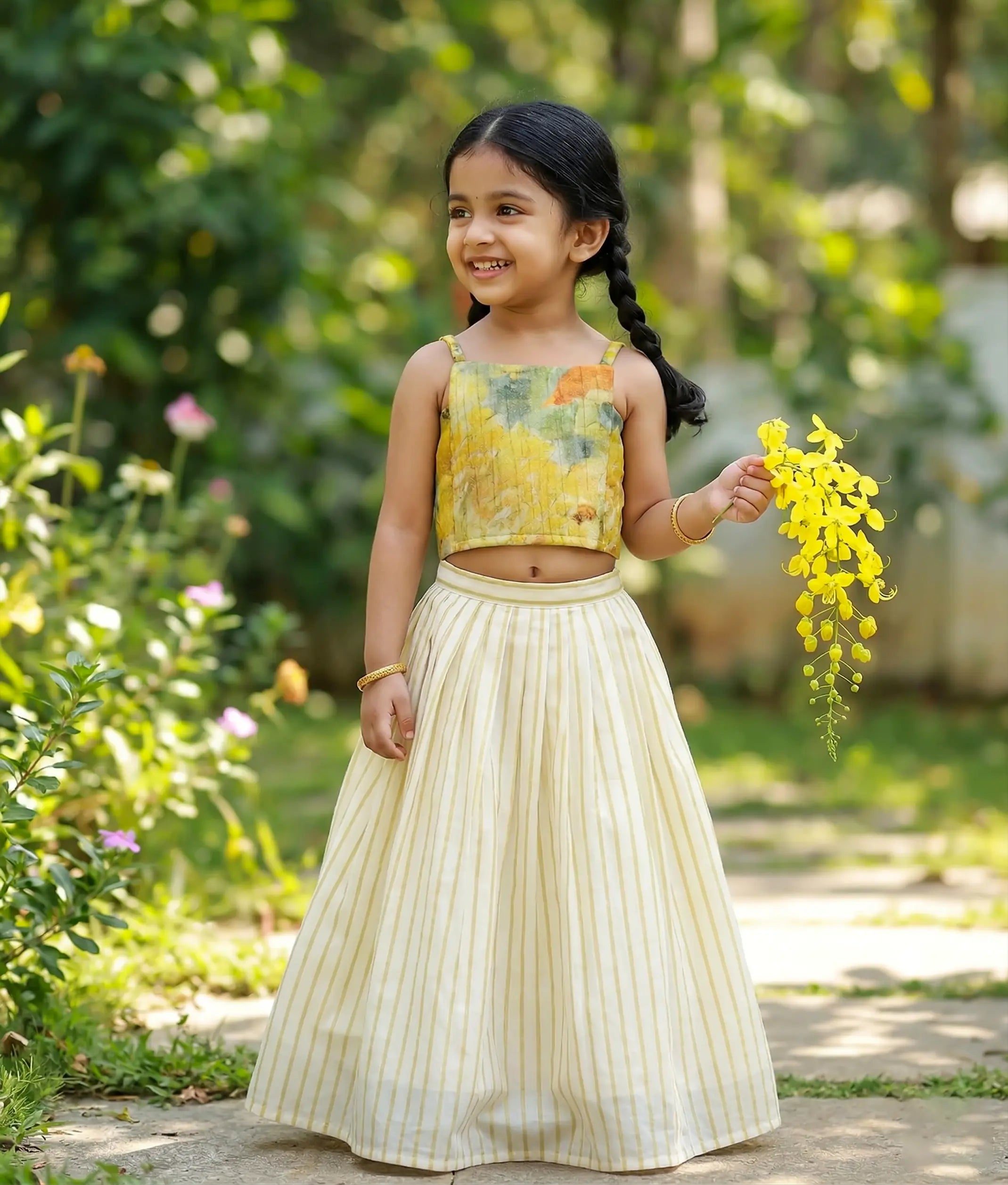 Baby girl wearing an ethnic set featuring a yellow floral silk top and a kasavu skirt with traditional gold kasavu stripes.