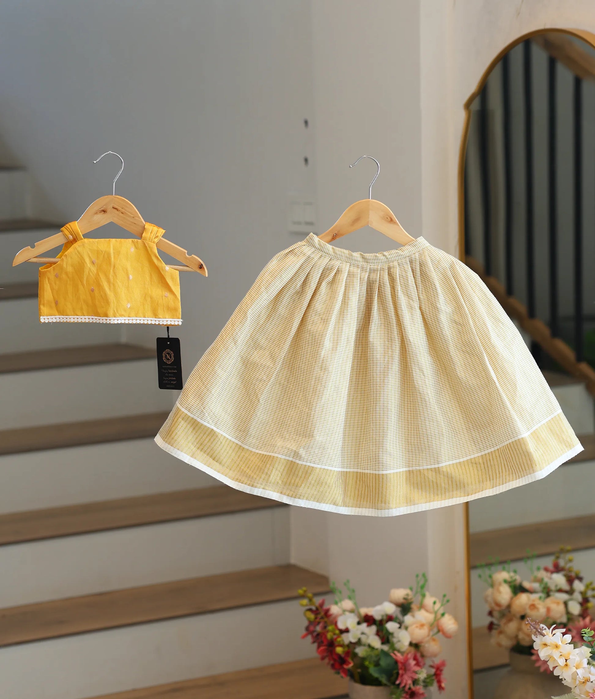 Front view of a girls' yellow top with lace trim and a cream pleated skirt with vertical stripes.